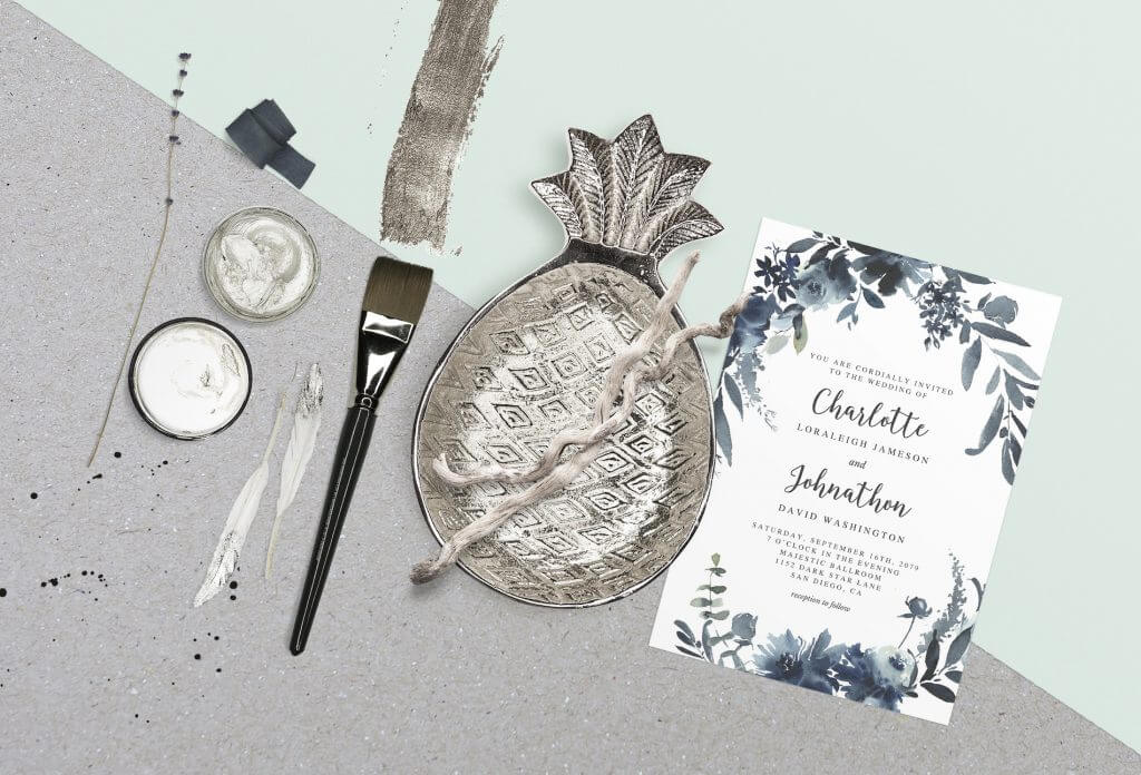 Art-Inspired Floral Wedding Invitation with Blueish Flower Illustrations and Elegant Font. Adjacent to a Silver Pineapple Plate, Paint Brush, and Paints.