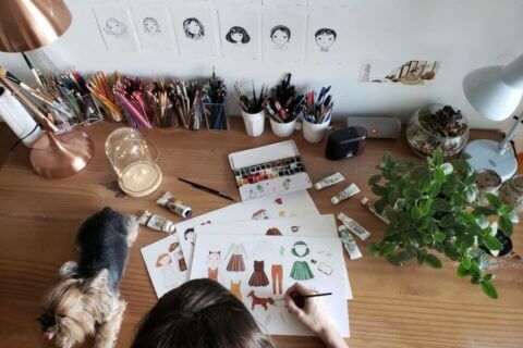 A woman sits at her desk, immersed in the creative process, as she designs watercolor motifs for her bespoke card and invitation collections.
