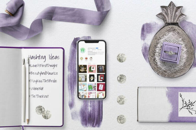 Wedding Planning Tools in Purple Hues: Open Notepad with Handwritten Hashtag Ideas, Smartphone, Silver Pineapple-Shaped Plate with Ring, and Coordinating Ribbon. Blog Post: 'Why Every Wedding Needs a Hashtag (and How to Create Yours)