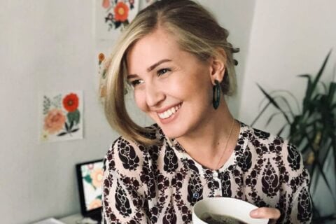 Portrait of artist Lisa Mönttinen in her studio, radiating joy with a warm smile, her hair styled in an elegant updo, amidst the creative serenity of her artistic workspace.