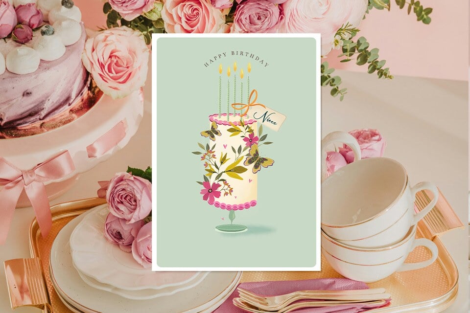 niece-birthday-card-cake-butterly-pastel (1) Pastel birthday card for a niece featuring an illustrated floral cake with candles and butterflies on a mint background, displayed in an elegant tea-party setting with pink roses, a frosted cake, teacups, and gold-accented tableware.