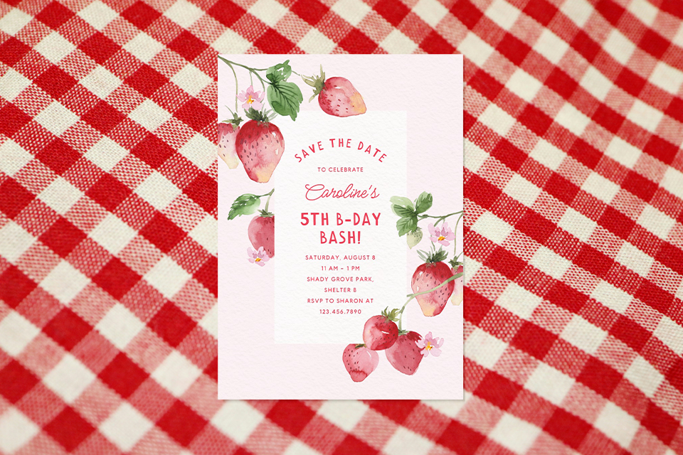 strawberry-theme-kids-birthday-invite Strawberry-themed kids’ birthday invitation with watercolor strawberries and flowers on a soft pink background, announcing a 5th birthday celebration, displayed on a red-and-white gingham picnic cloth.