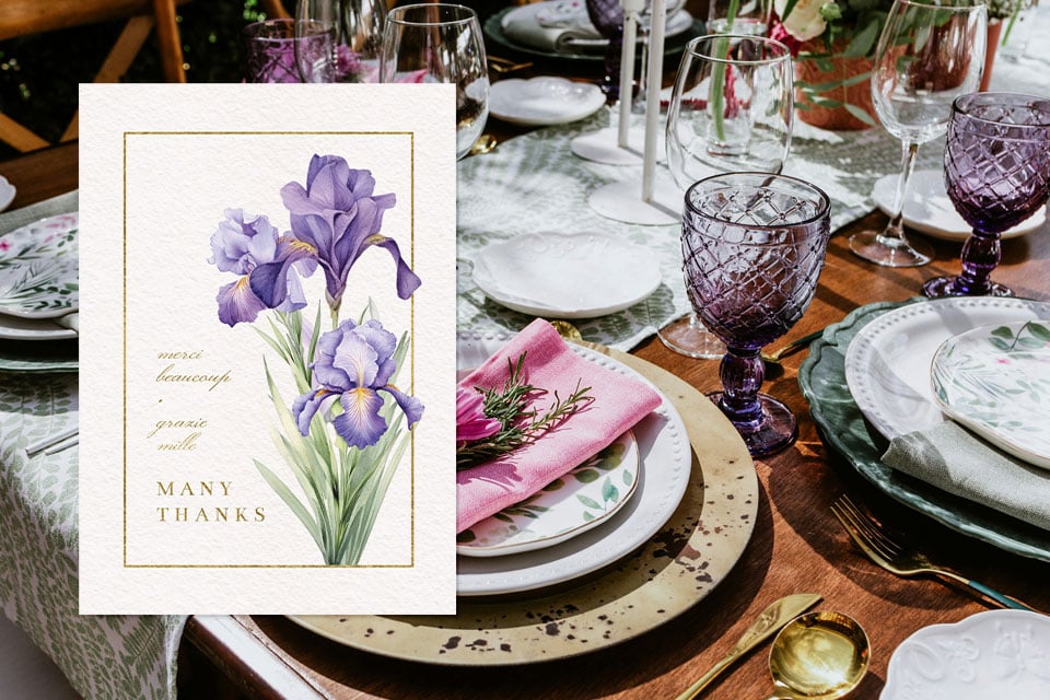 wedding-anniversary-thank-you-card Floral thank-you card featuring purple iris illustrations displayed on an elegantly set dining table with layered plates, glassware, and pink napkin accents.