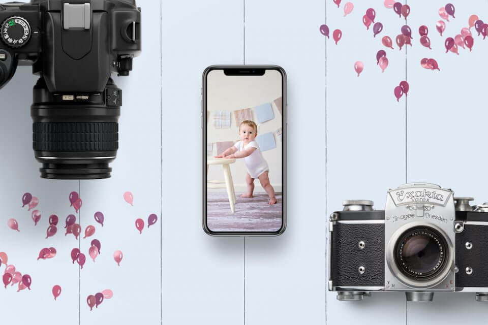 Composition of an iPhone with Baby Photo, Professional Modern Camera, and Vintage Camera on a Light Blue Wooden Surface.