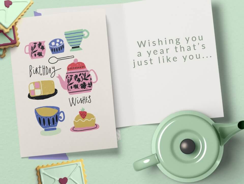 Birthday Wishes and Whimsical Card Illustrations Featuring Teapot, Cups, and Cake, Set Against a Clean White Background. Positioned on a Light Green Surface, Accompanied by an Open Card and a Charming Teapot.