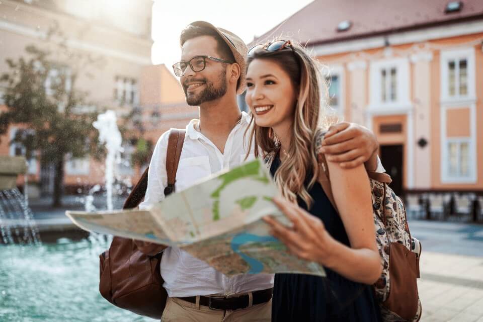Smiling couple exploring a charming town with a map in hand, enjoying a romantic adventure together during their anniversary trip.
