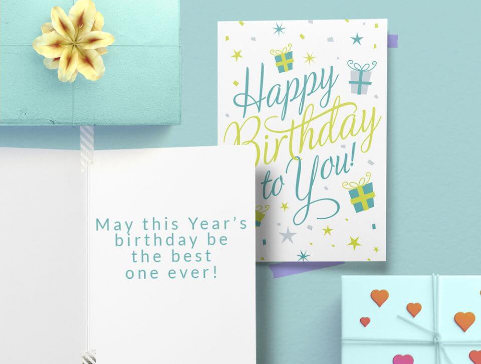 Pastel Script Birthday Card: 'Happy Birthday to You' in Gentle Green and Blue Tones, Adorned with Illustrations of Wrapped Gifts and Delicate Stars. Resting on a Subtle Blue Background, with an Open Card and Wrapped Gift Nearby.