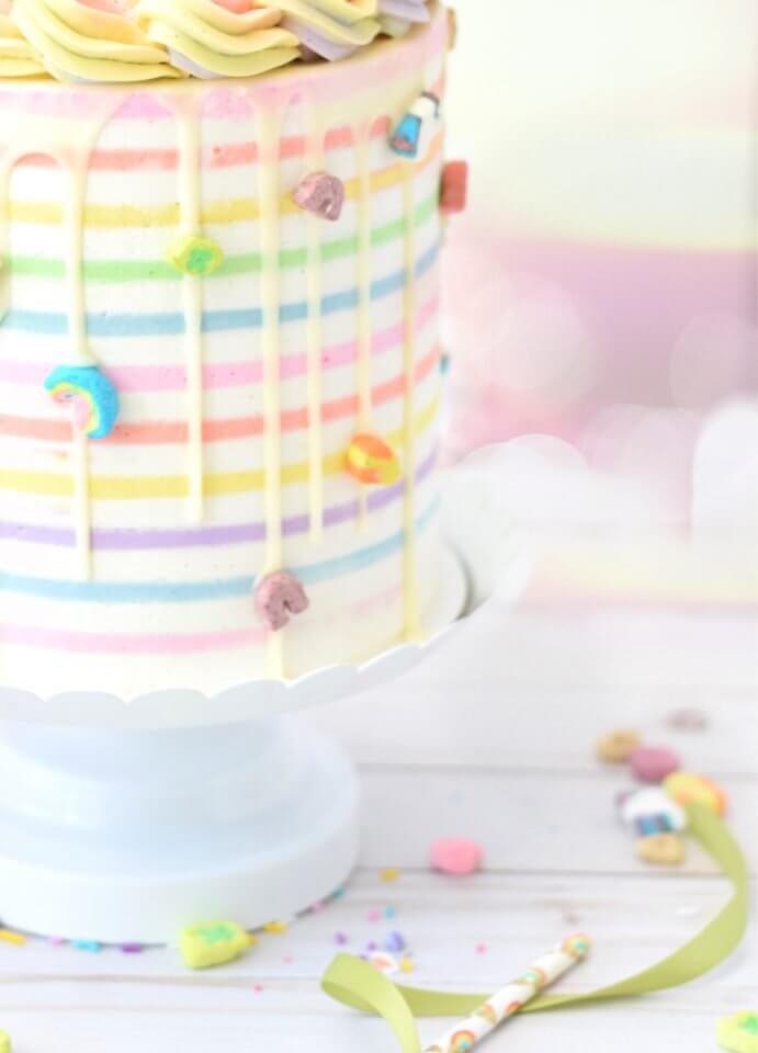 Rainbow cake featuring layers of vibrant colors and dripping icing adorned with assorted candy in various shapes.