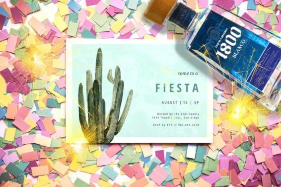 Fiesta invitation featuring a charming cactus design, placed atop a bed of colorful confetti and positioned near a festive bottle of drink