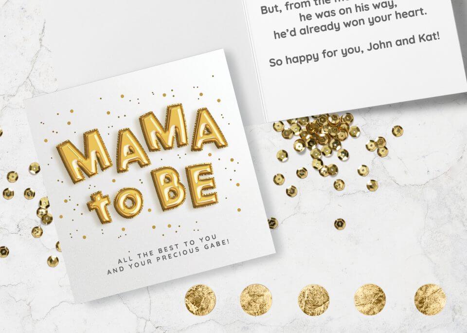 Heartfelt 'Mama to Be' New Baby Card with golden balloon-style text, set on a surface adorned with shimmering golden sequins.