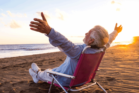 Senior man relaxing on beach chair at sunset with arms wide open, enjoying peaceful summer vacation by the ocean.