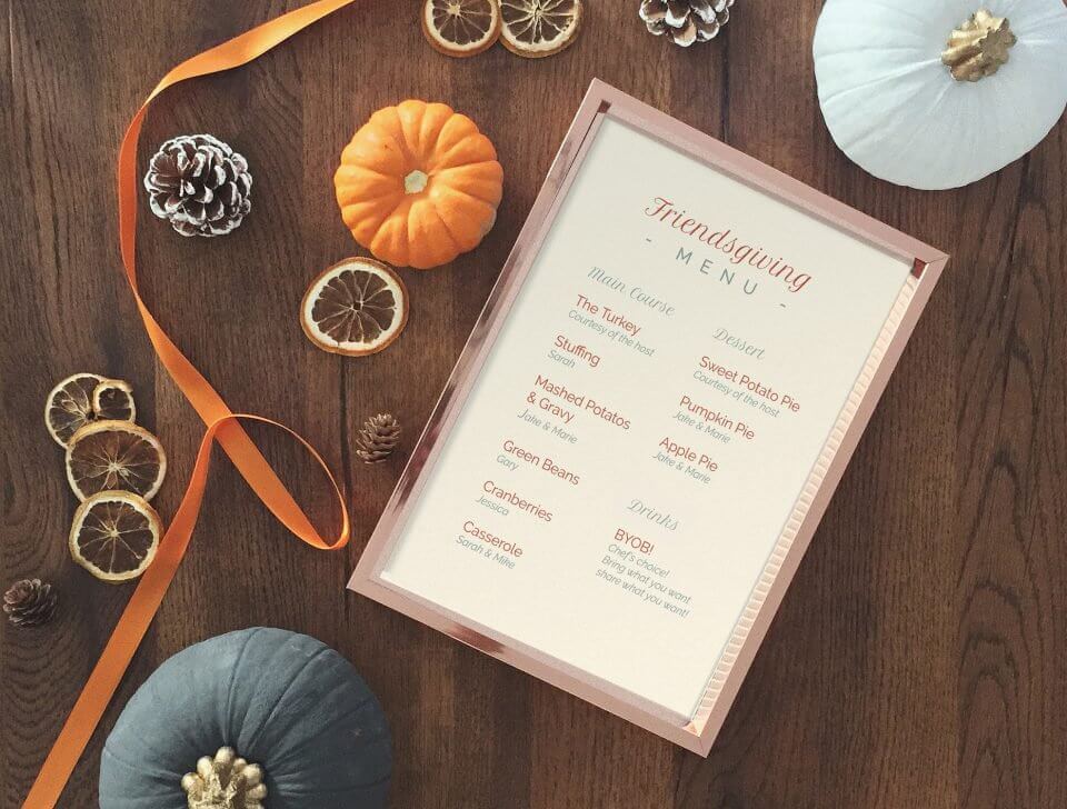 Friendsgiving Menu on Red Gold Frame, Resting on Wooden Table with Dried Oranges, Pumpkins, and Pine Cone.