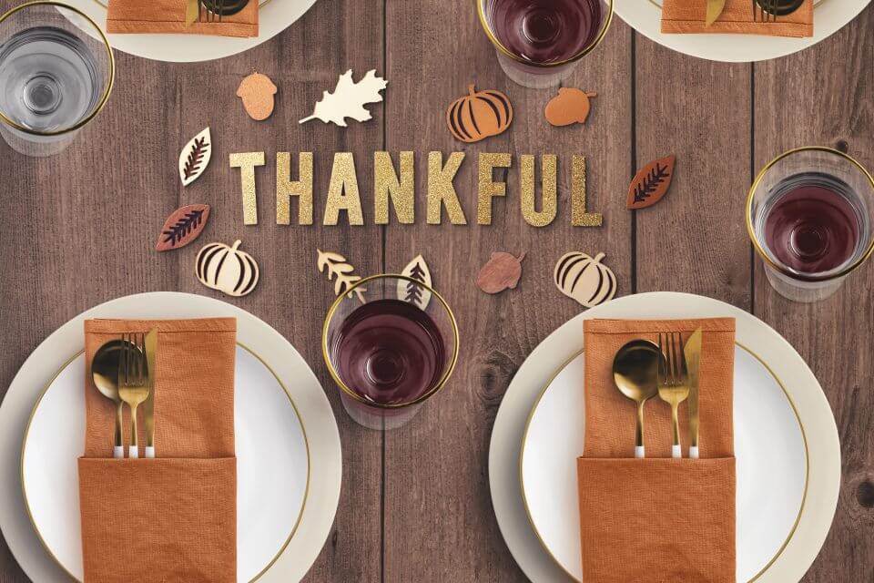 table centrepiece featuring 'Thankful' inscription. Two plates with dark orange napkins and golden utensils set in an elegant arrangement.