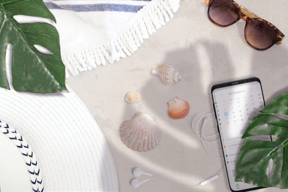 
Navigating the Virtual Business Party: Revel in the joy of online festivities with a smartphone resting on sand amidst shells, sunglasses, and a sun hat—a perfect blend of work and leisure.