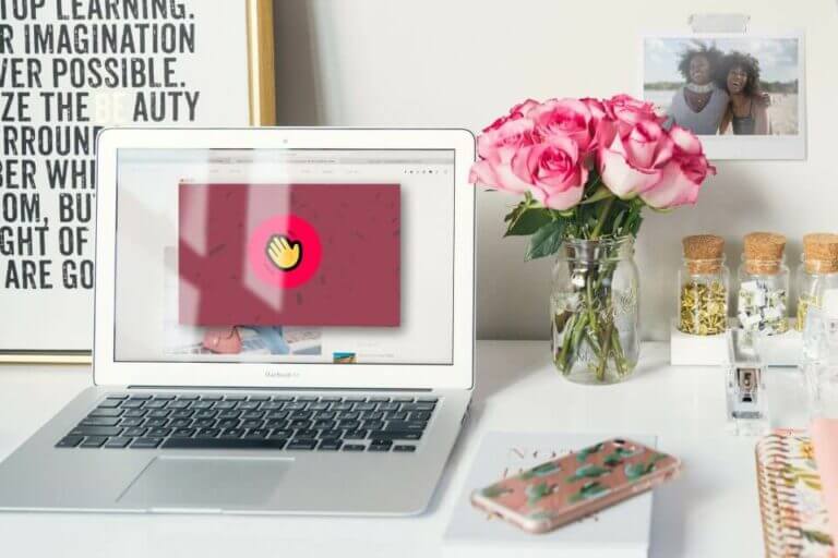 Laptop displaying a virtual meeting on its screen, accompanied by a vase of roses and a notebook nearby.