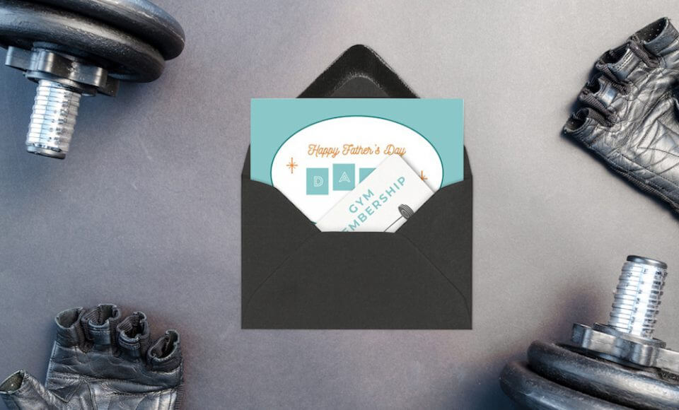 A gym membership gift for Father's Day, presented as a card inside a black envelope, with gym equipment placed nearby. This image conveys the thoughtful gift idea of a gym membership for dad to celebrate Father's Day and promote his health and fitness.