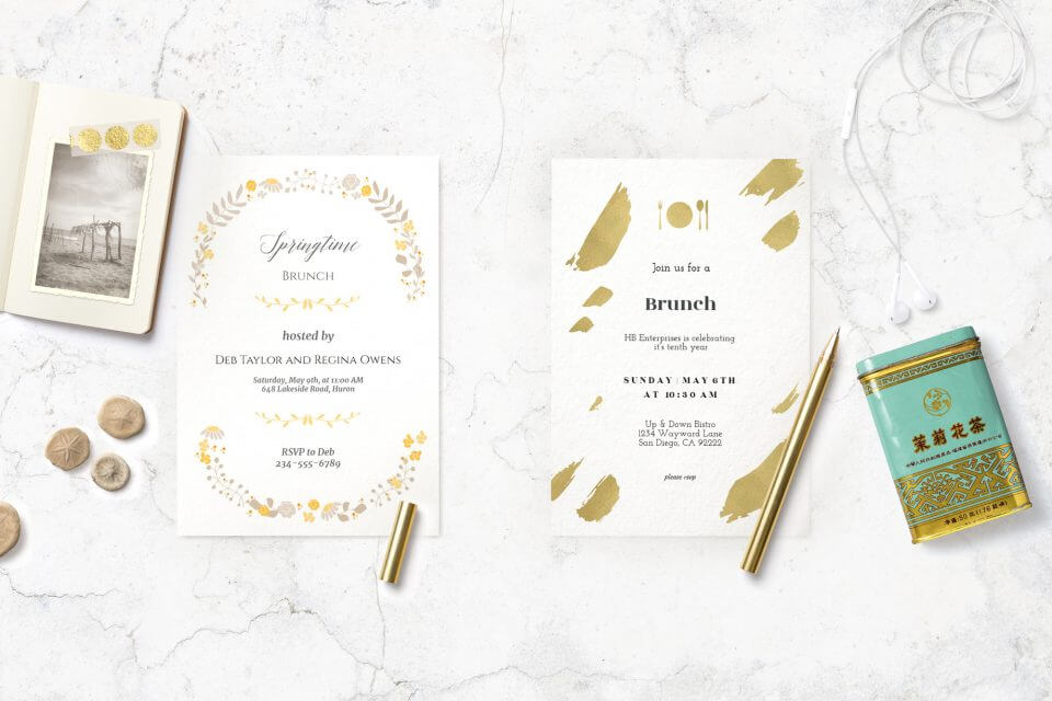 Stylish Brunch Invitations: Adorned with golden accents, one featuring elegant brush strokes and the other with ornate illustrations, they rest side by side on a sleek granite surface. Accompanied by a golden pen and a notebook