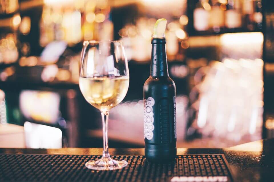 A charming scene set in a cozy bar, featuring a bottle of wine alongside a glass of white wine, elegantly arranged on the bar counter. 