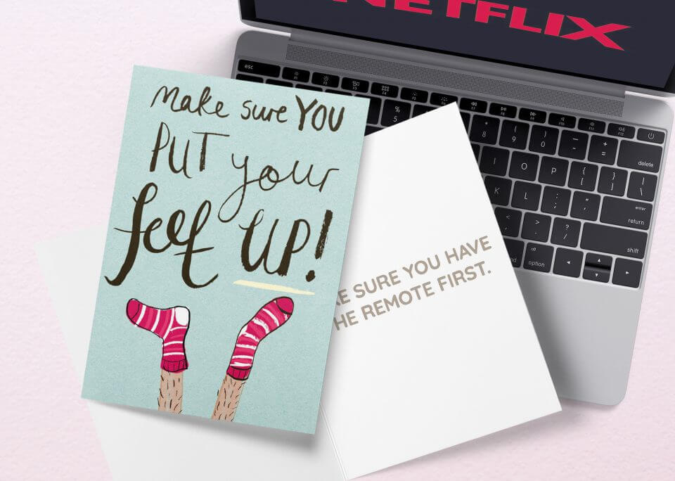 A 'Best Get Well Wishes & Quotes For A Speedy Recovery' greeting card titled 'Put Your Feet Up', featuring an illustration of feet donning red socks, is thoughtfully placed atop a laptop keyboard. The unique placement and the playful imagery of the card convey a message of relaxation and taking a break, aligning with the theme of recovery and well-being.