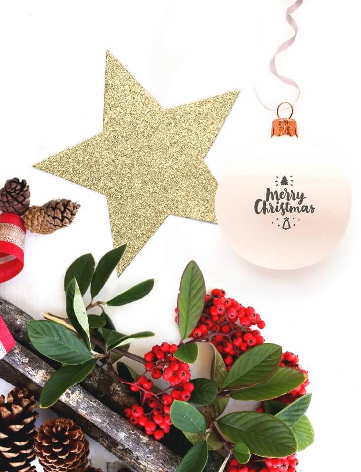 Merry Christmas ornament delicately positioned on a pristine white surface, adorned with a shimmering golden paper star and accompanied by a lush Christmas greenery branch
