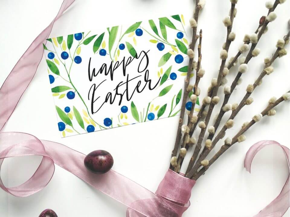 Wishing you a Happy Easter with a delightful card adorned by a watercolor illustration of blooming blueberry branches. The card, set on a pristine white surface, features a charming arrangement with a tiny egg and budding flowers, evoking the essence of springtime renewal and celebration.