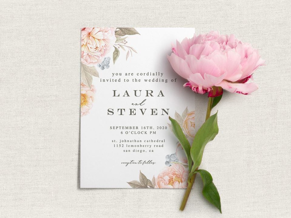 Peach Flowers Wedding Invite: Delicate peach blooms adorn corners, complemented by deep green text. Resting on a light grey surface, crowned by a pink blossom.