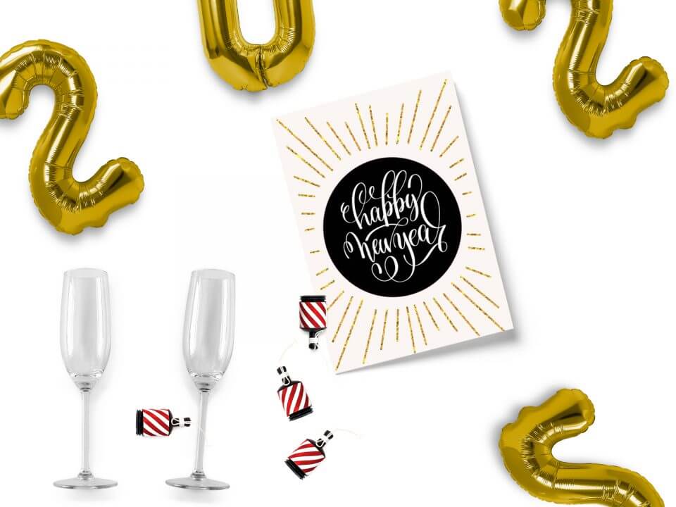 A joyous Happy New Year card featuring a striking sun design with a bold black sun and radiant golden rays, harmoniously placed alongside white text in the center. Enhancing the celebratory scene are vibrant number balloons and elegant champagne glasses.