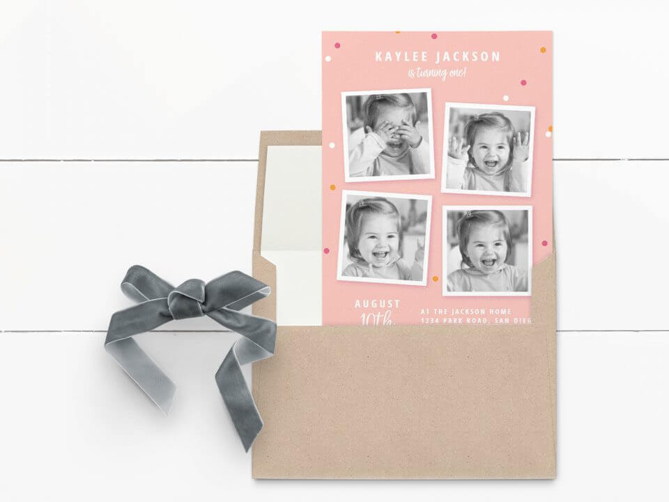 Multi-Photo First Birthday Invitation: Light Pink with Pink, Orange, and White Dots, Featuring Black and White Photographs. Resting on an Open Envelope, Accented by a Grey Velvet Bow.