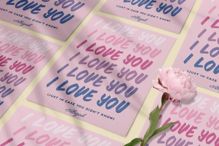 Love You" Repeated in Various Gradient Colors on a Pink Background Card. Multiple Cards Arranged on a Surface with a Blooming Flower. Cover for '100+ Romantic Love Messages & Wishes.