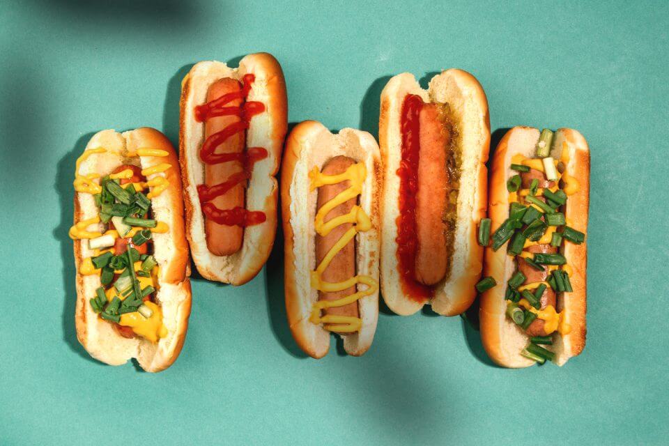 An enticing array of uniquely styled hot dogs presented on a vibrant green surface, offering delicious inspiration for a sports-themed party spread that combines culinary creativity with game day excitement.