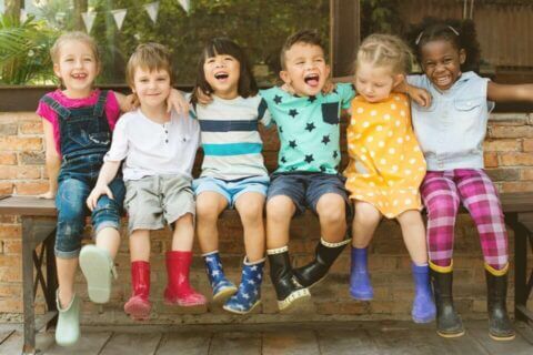 Children seated on a bench outdoors, enjoying a day filled with laughter and fun. Their colorful clothes and rain boots adding a vibrant touch to the joyful moment.