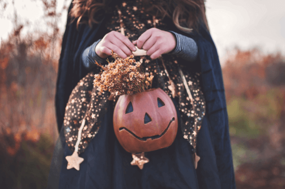 A young girl in a witch costume holding a jack-o'-lantern pumpkin for halloween party