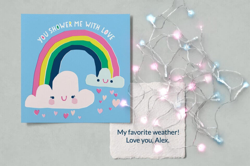 Sunny Rainbow Love Card for Valentine's Day. A cheerful rainbow and clouds illustration on a blue background, with hearts pouring out, and the heartfelt message: 'You shower me with love'