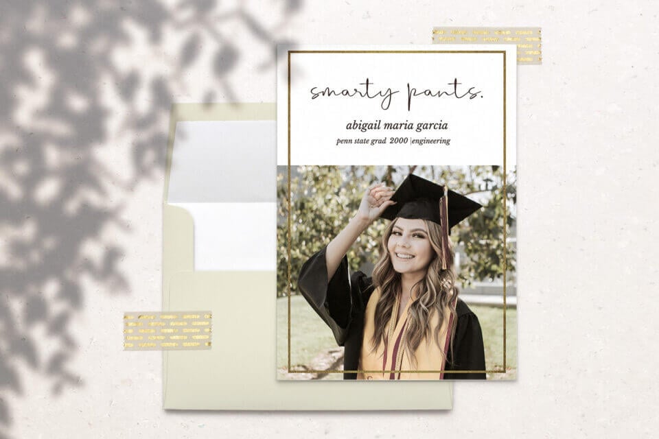 A Gold and Cream Graduation Announcement card and its coordinating envelope, where the card showcases a prominent photograph of a woman confidently wearing a graduation cap. 
