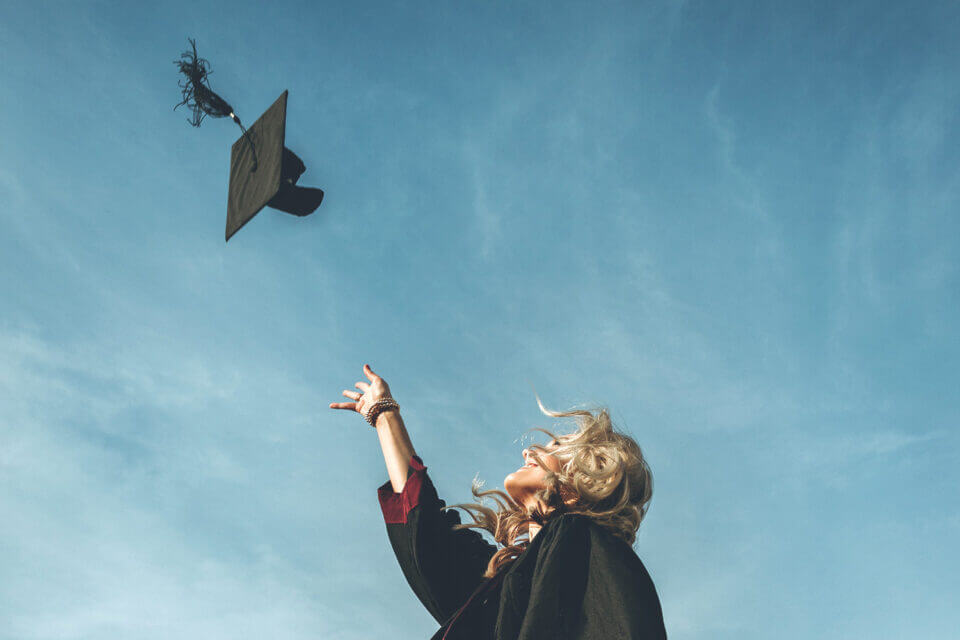 A photograph capturing a moment at a graduation party where a graduate is joyously throwing her cap into the air. The image conveys a sense of achievement and celebration