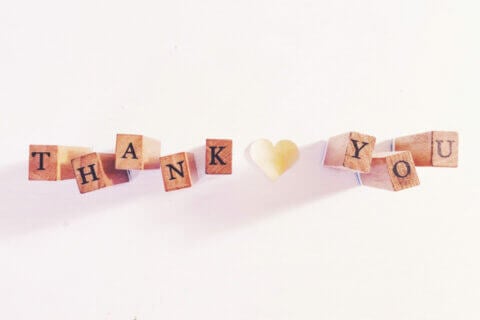 Wooden blocks spell 'THANK YOU' with a paper heart. Clear display on white background. Warm and sincere. Cover for 'How To: Wedding Thank You Cards Wording Ideas'