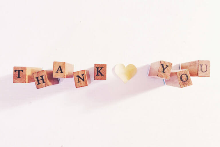 Wooden blocks spell 'THANK YOU' with a paper heart. Clear display on white background. Warm and sincere. Cover for 'How To: Wedding Thank You Cards Wording Ideas'