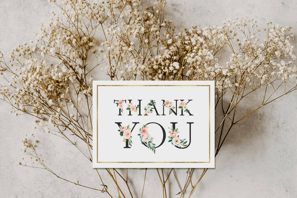 Elegant wedding thank you card with golden text adorned by delicate flowers. Golden border adds sophistication. Rests on a bed of dried baby's breath flowers.