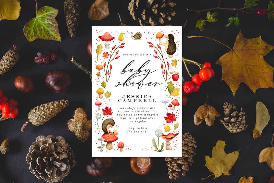 Charming baby shower invitation featuring adorable hedgehog and apple illustrations, complemented by autumnal hues of mushrooms. Resting on a backdrop of a flat lay with leaves and pine cones, evoking the cozy essence of fall.