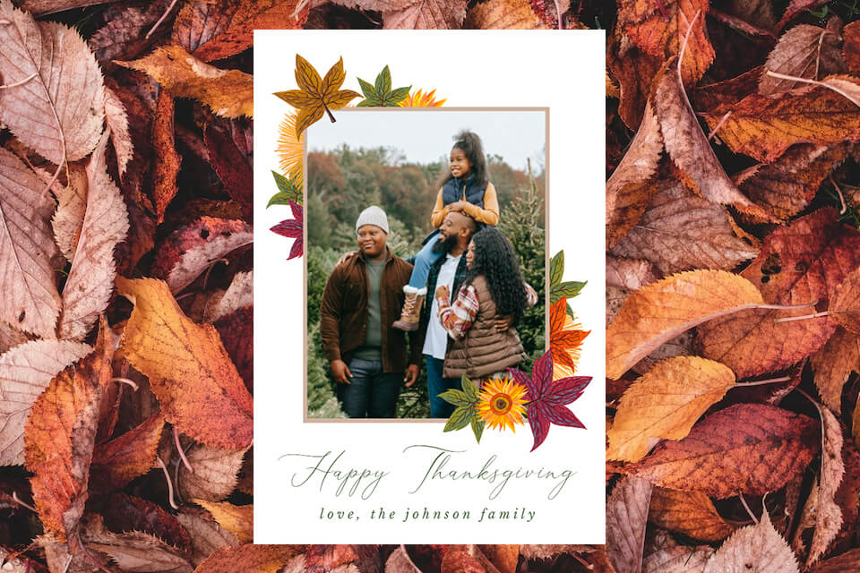 Happy Thanksgiving card featuring a family of four in a photo frame, surrounded by autumn leaves. The card rests on a background of fallen autumn leaves, creating a warm and inviting atmosphere for the holiday season.