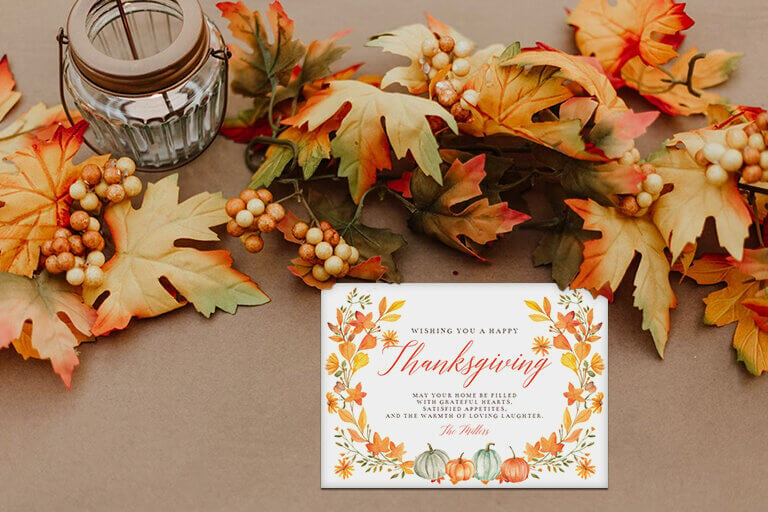 Thanksgiving card with text wishing you a happy thanksgiving. The invite fatures illustration of yellow foliage and pumpkins. The invitation is placed on a table decorated with autumn leaves and a latern. this is the cover for blog post 25 Thanksgiving Wishes Ideas For a Happy Holiday