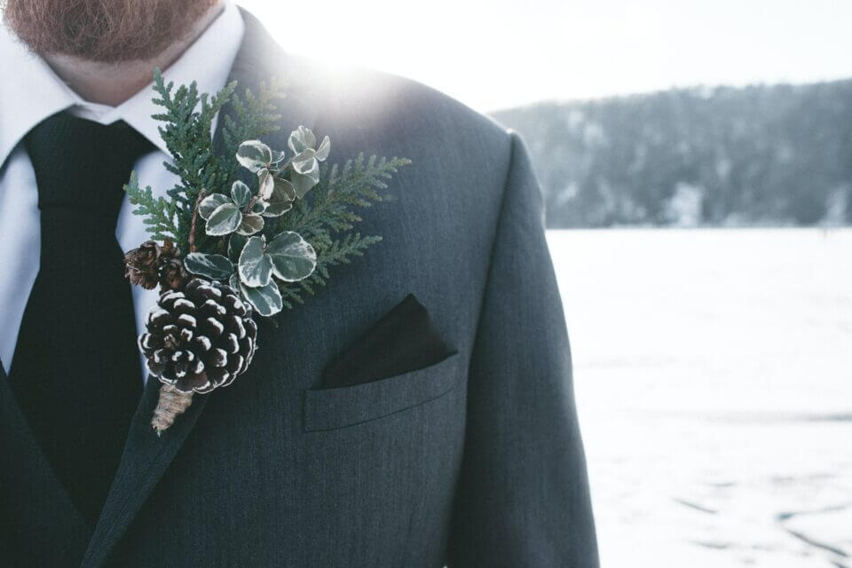 Winter wedding: Close-up of the groom outside amidst the snow, with a stunning flower arrangement in focus.