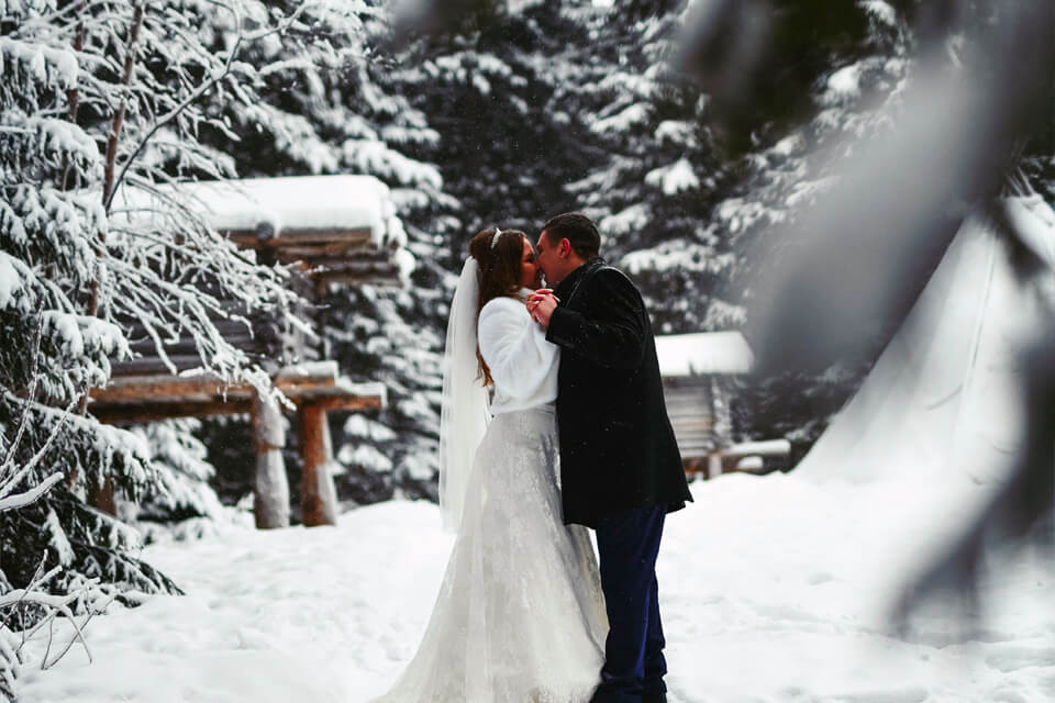Romantic Winter Wedding Moment: Bride and Groom Sharing a Kiss in the Snowy Outdoors, Resplendent in Wedding Attire.