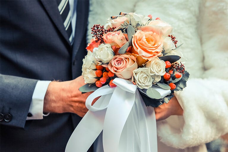 Bride and groom holding a beautiful bouquet of flowers. cover for the blog post '16 Magical Christmas Wedding Ideas Guests Will Never Forget'.