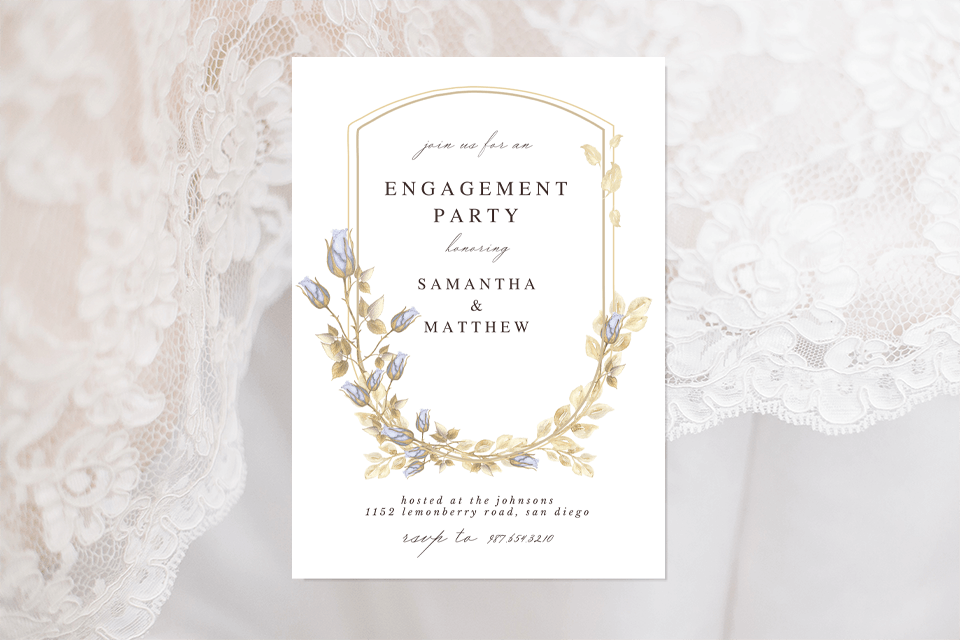 An elegant engagement party invitation featuring a gold and light blue floral shield illustration. The invite is set against a backdrop of delicate white lace fabric