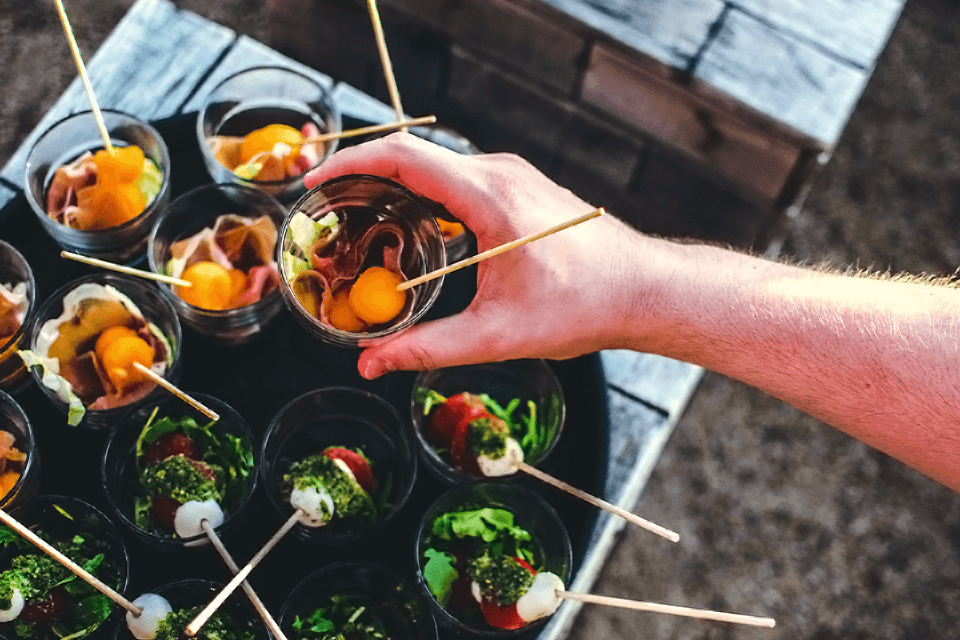 Artfully arranged party finger foods with a hand delicately selecting a delectable treat.