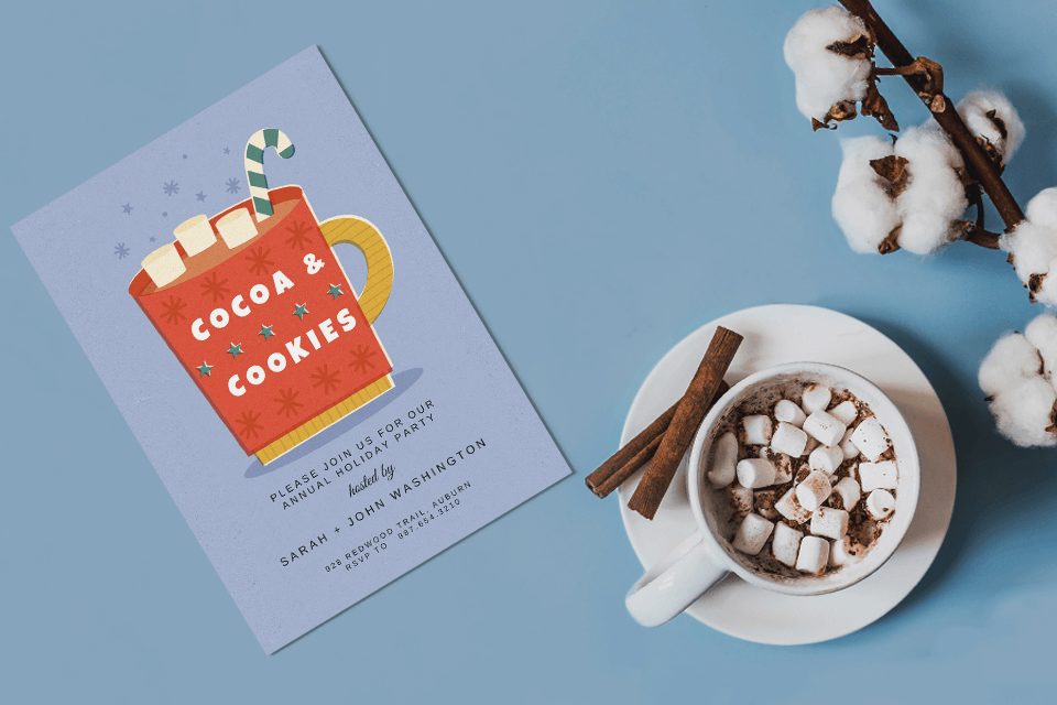 cocoa and cookies party invitation laying on table top with a cup of hot cocoa 