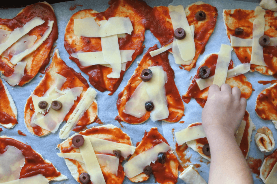 a child arranging pizza toppings on heart shaped pizzas for valentine's day