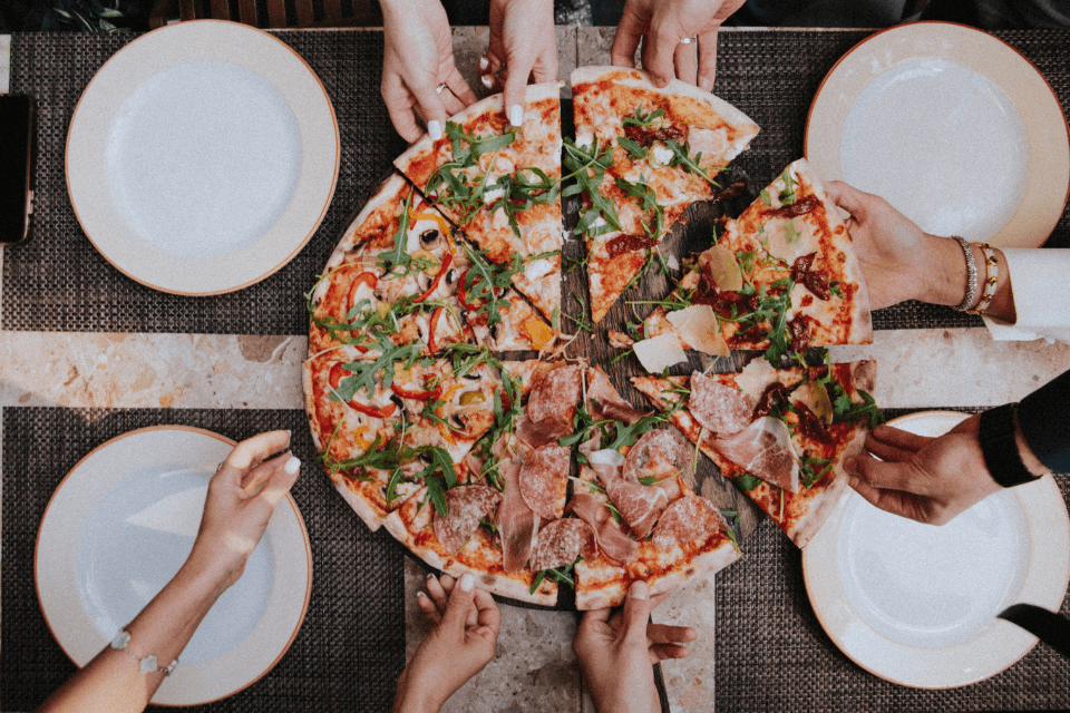 An overhead shot of a large, inviting pizza with a variety of toppings, as people's hands reach in from all sides to grab a slice, capturing a moment of communal enjoyment.