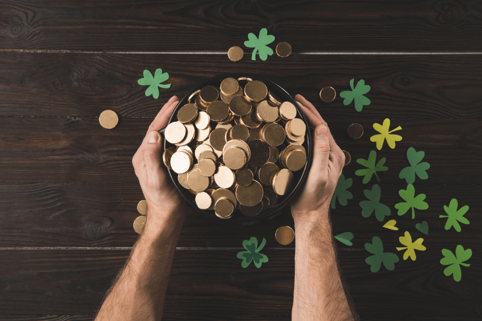 St. Patrick's Day symbols person holding pot of gold with lucky clover décor scattered around